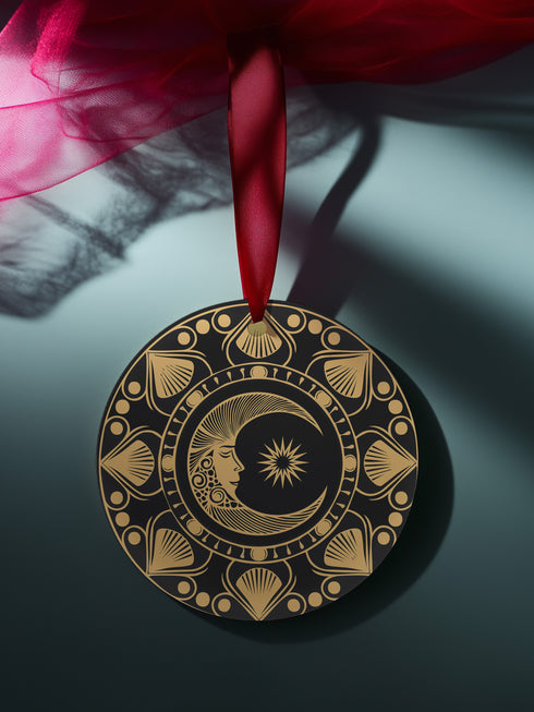 Round metal ornament featuring a golden crescent moon face with star detail, surrounded by art deco shell motifs on black background. 3.5-inch diameter double-sided design with lunar phase pattern and crimson ribbon attachment. Vintage-inspired celestial artwork.